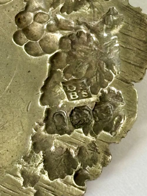 fig 1. A George III sterling silver decanter label engraved with MADEIRA, decorated with a chased mask of Bacchus, grapevines, and an attached suspension chain.