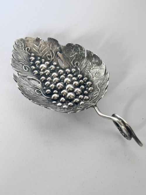 fig 1. A George III sterling silver caddy spoon fashioned as a vine leaf with an embossed grape cluster and a wire loop handle.