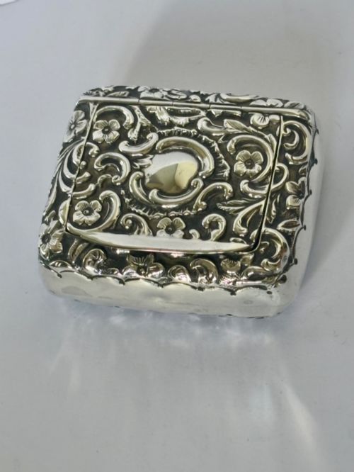 fig 1. A Victorian rectangular sterling silver snuff box with heavily embossed floral and scroll decoration surrounding a plain central cartouche.