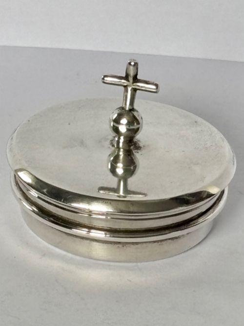 fig 1. A circular sterling silver pyx box with a polished finish, featuring a lid topped with a cross and orb finial.