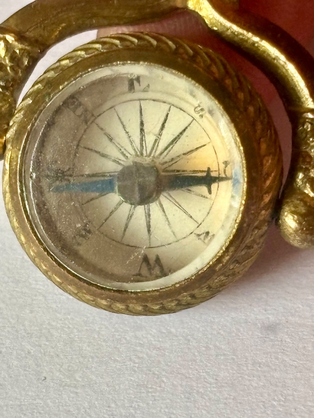 An antique Victorian gilt metal swivel compass fob pendant featuring a textured suspension arch, a rope-twist border, and a compass dial beneath glass. View II