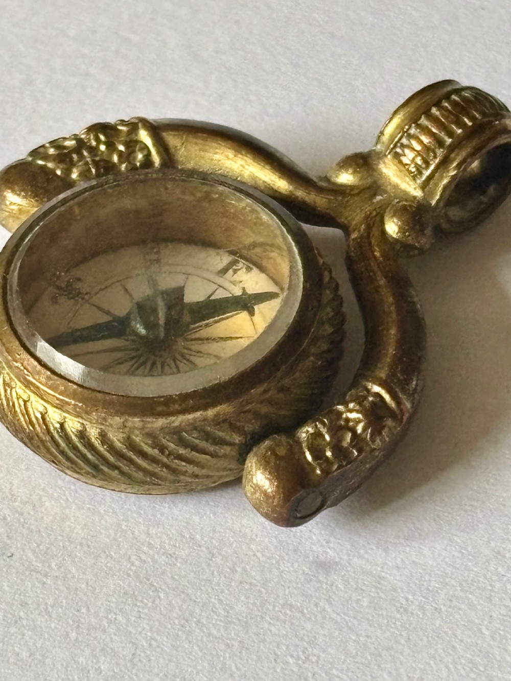 An antique Victorian gilt metal swivel compass fob pendant featuring a textured suspension arch, a rope-twist border, and a compass dial beneath glass. View V