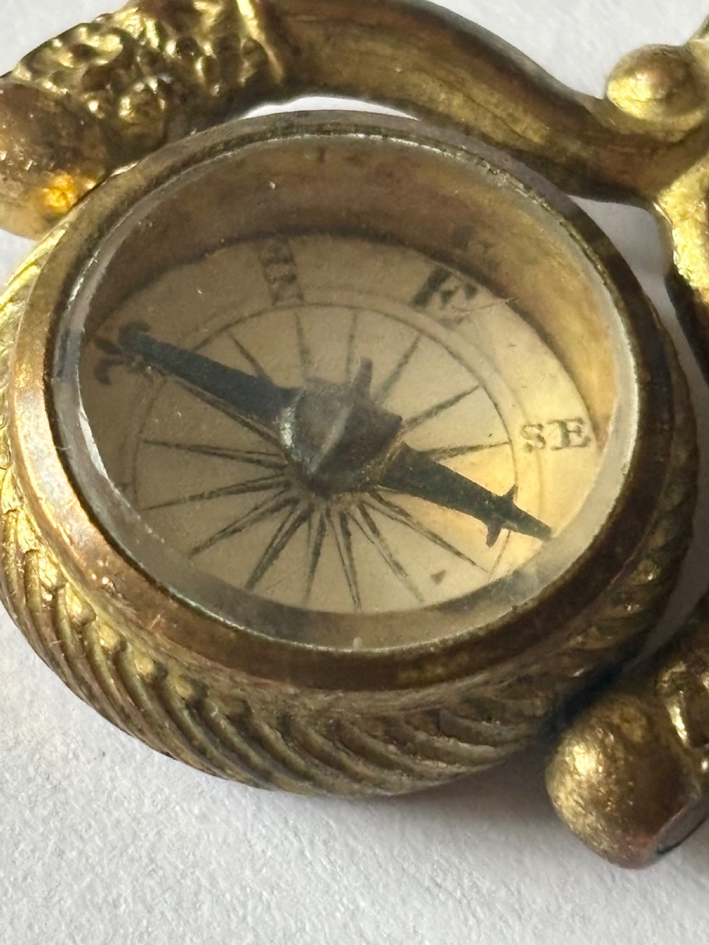 An antique Victorian gilt metal swivel compass fob pendant featuring a textured suspension arch, a rope-twist border, and a compass dial beneath glass. View VI