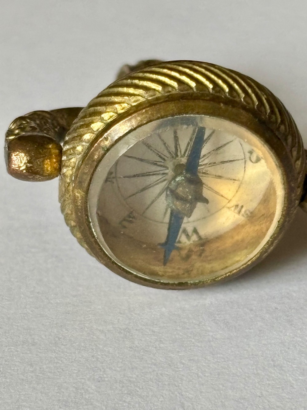 An antique Victorian gilt metal swivel compass fob pendant featuring a textured suspension arch, a rope-twist border, and a compass dial beneath glass. View VII