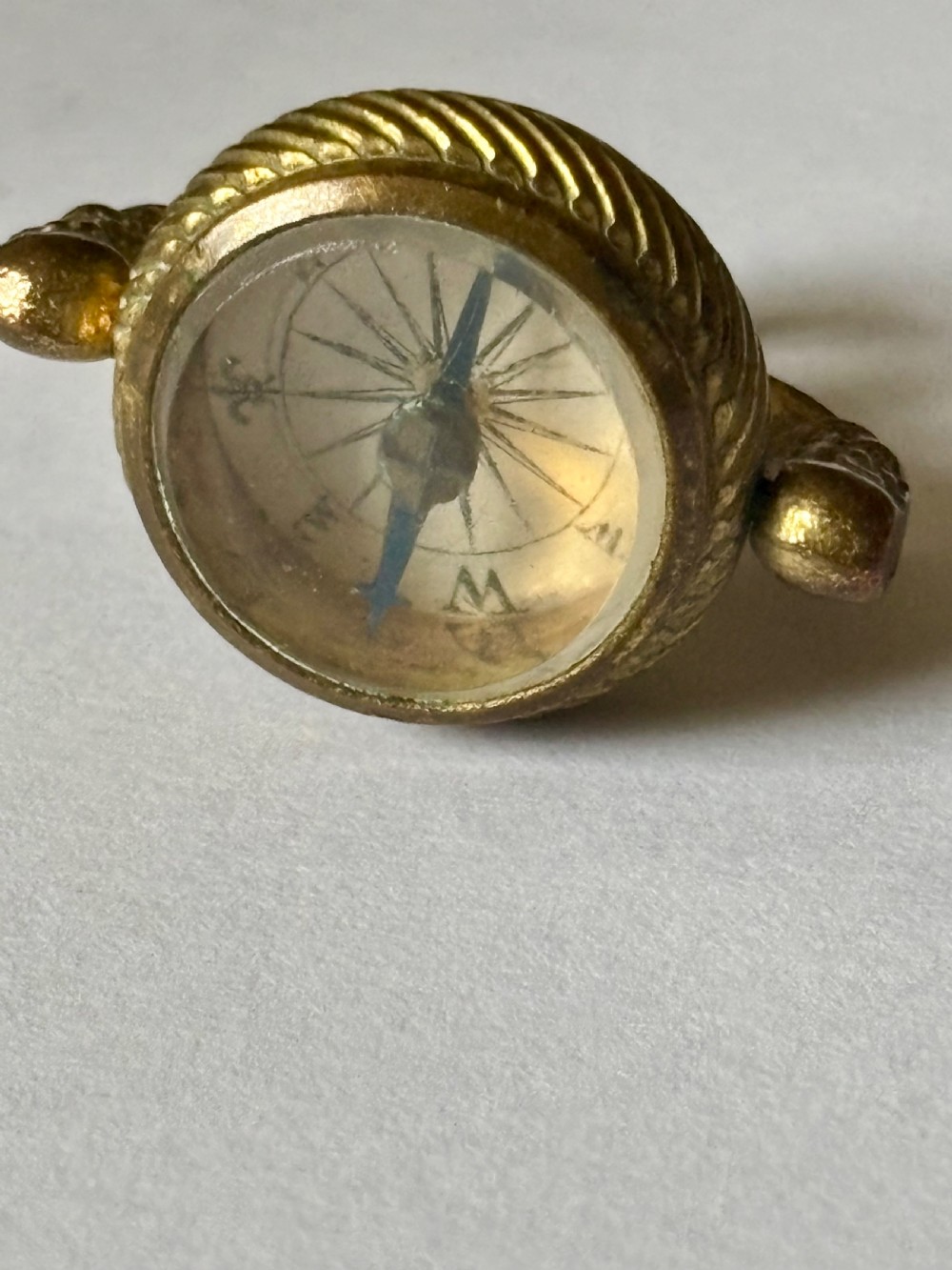 An antique Victorian gilt metal swivel compass fob pendant featuring a textured suspension arch, a rope-twist border, and a compass dial beneath glass. View VIII