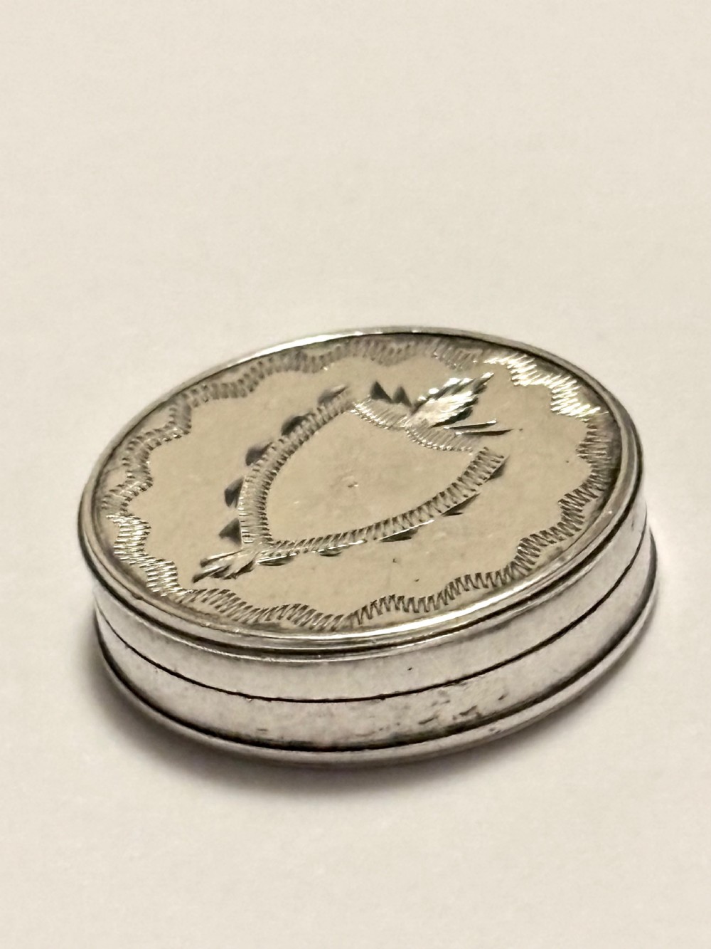 An oval George III sterling silver patch box featuring hand-engraved bright-cut decoration with a central shield motif.