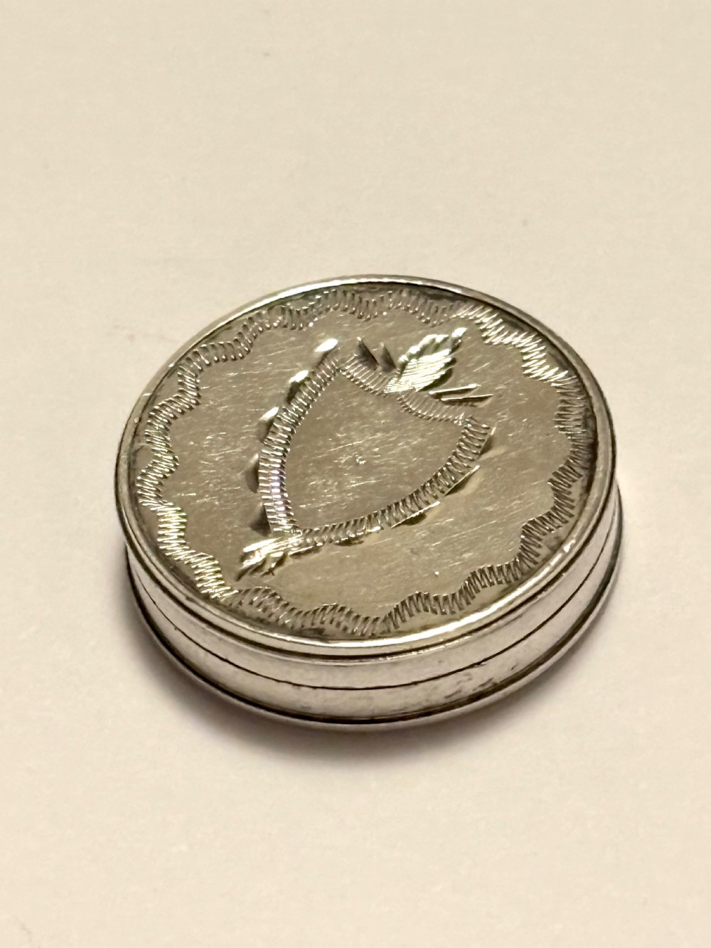 An oval George III sterling silver patch box featuring hand-engraved bright-cut decoration with a central shield motif. View II