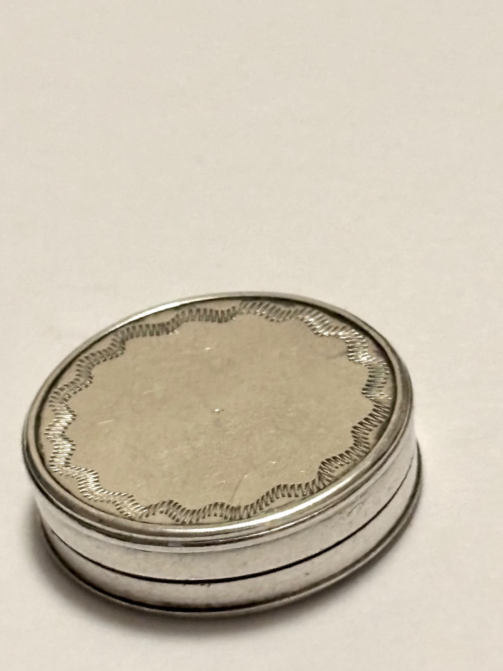 An oval George III sterling silver patch box featuring hand-engraved bright-cut decoration with a central shield motif. View III