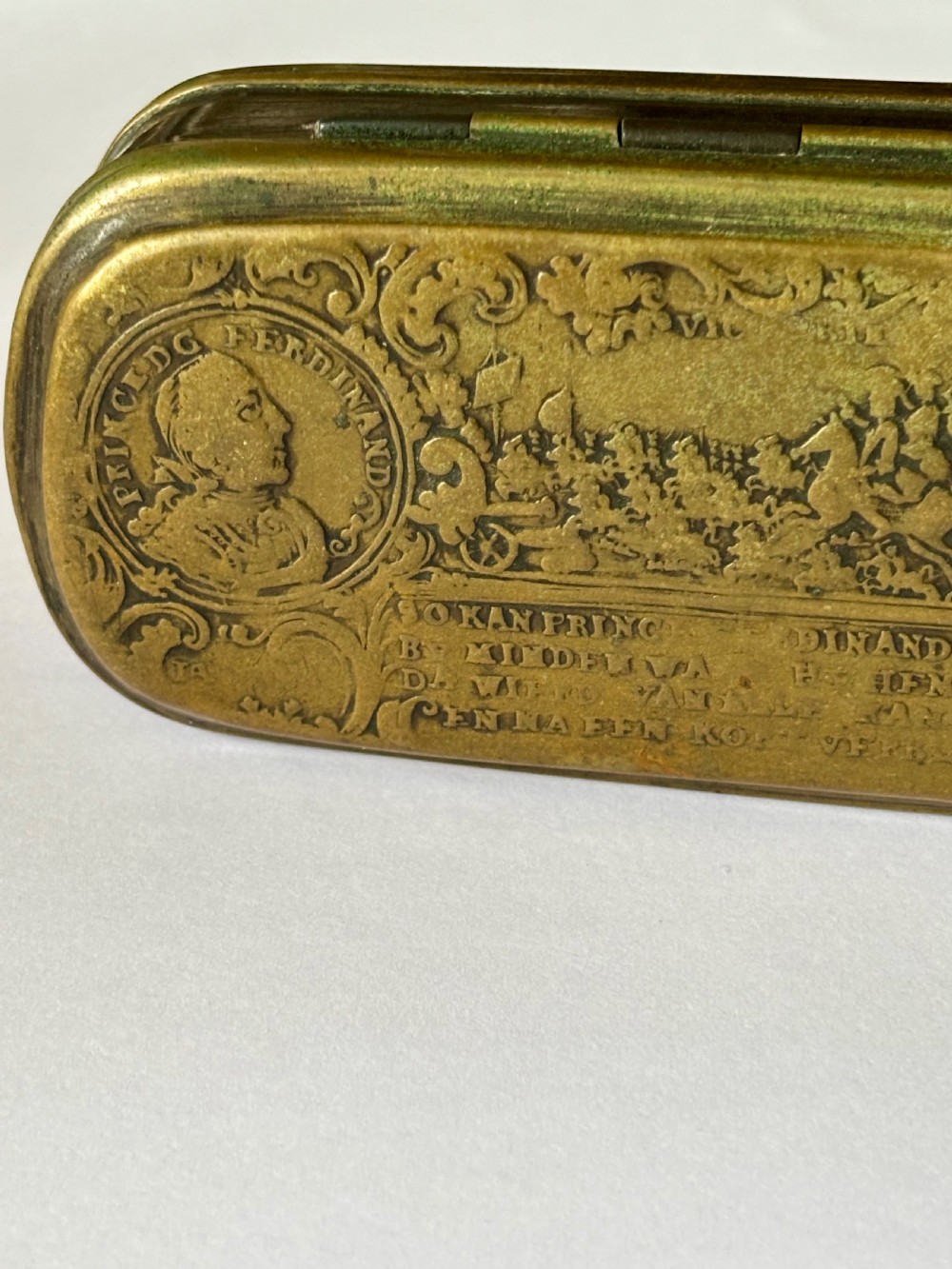 An oblong 18th-century brass and copper tobacco box featuring relief engravings of military battle scenes and portrait medallions on its lid. View V