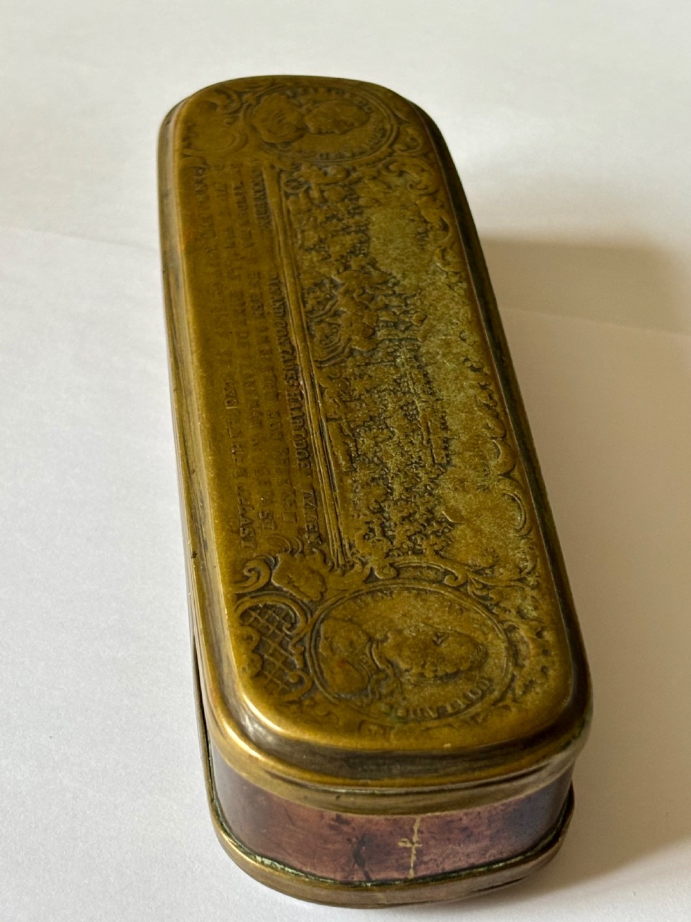 An oblong 18th-century brass and copper tobacco box featuring relief engravings of military battle scenes and portrait medallions on its lid. View IX