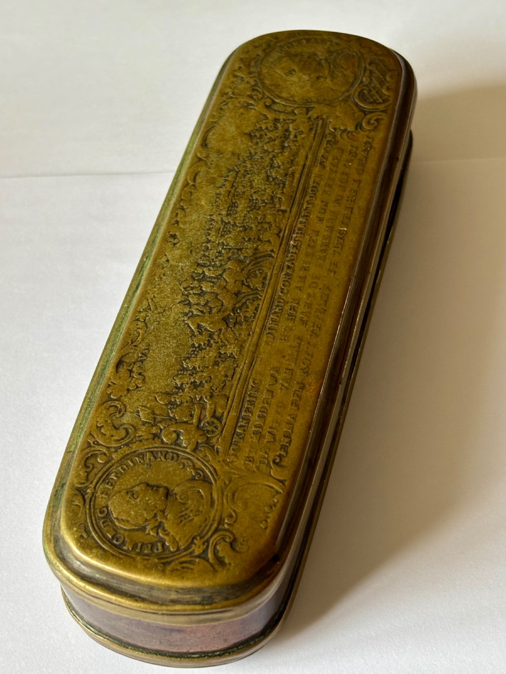 An oblong 18th-century brass and copper tobacco box featuring relief engravings of military battle scenes and portrait medallions on its lid. View X