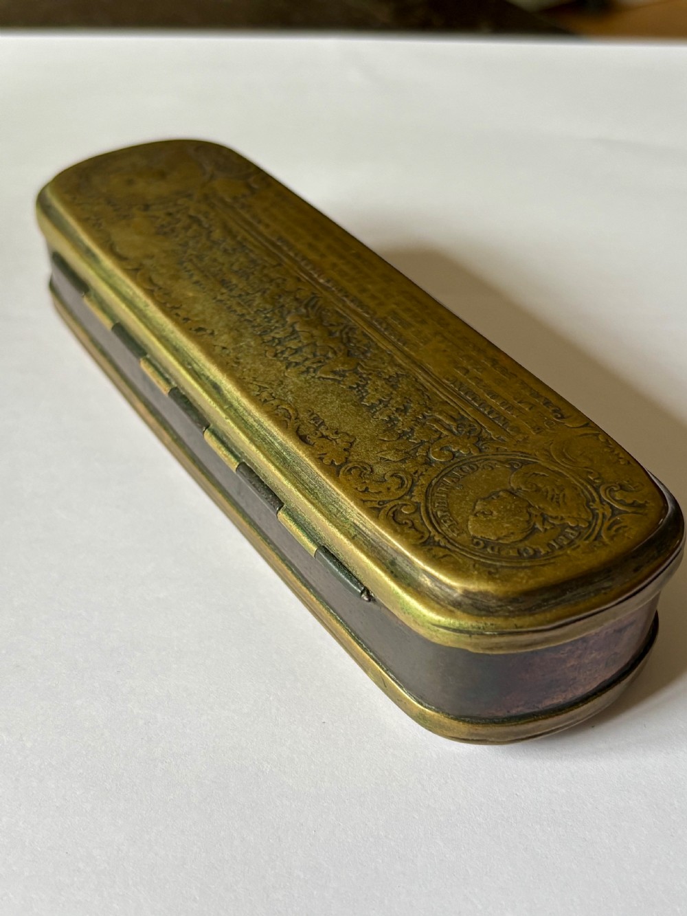An oblong 18th-century brass and copper tobacco box featuring relief engravings of military battle scenes and portrait medallions on its lid. View XVIII