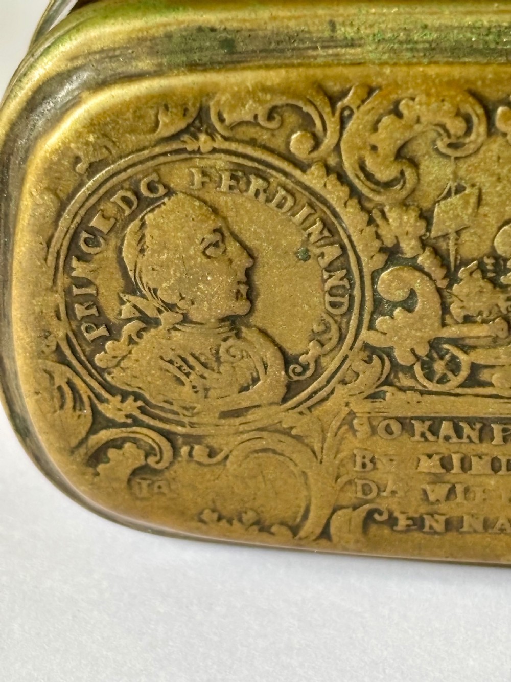 An oblong 18th-century brass and copper tobacco box featuring relief engravings of military battle scenes and portrait medallions on its lid. View XX