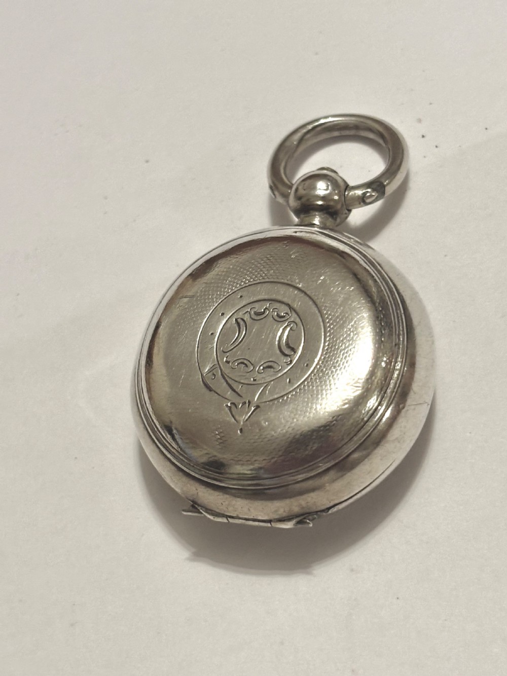 A circular Victorian sterling silver sovereign case with hand-engraved scrollwork detail and a top suspension loop.