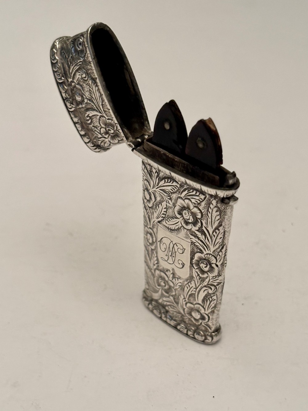 An open William IV sterling silver fleam case with floral chasing, revealing two dark-handled folding blades inside.