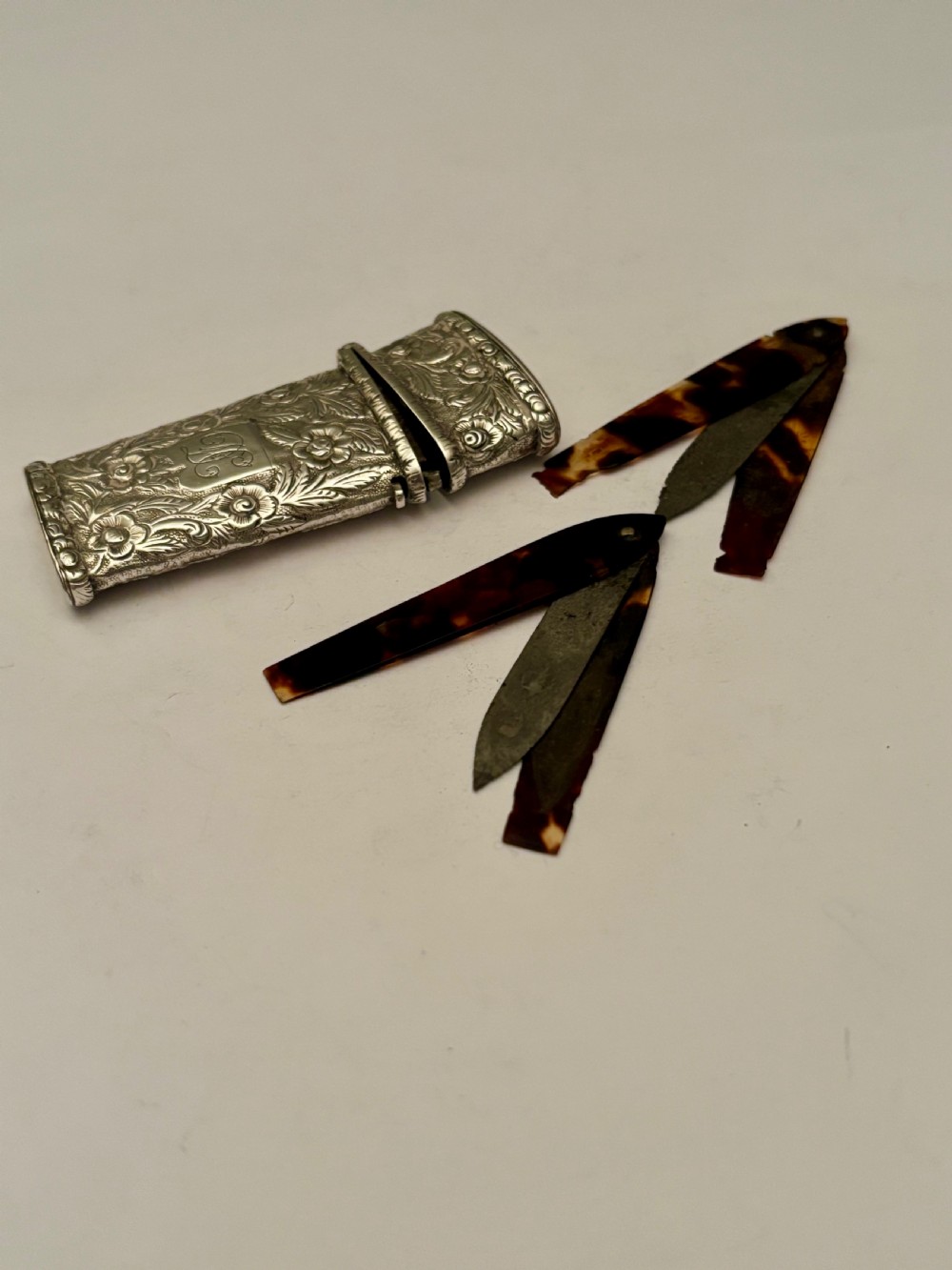 An open William IV sterling silver fleam case with floral chasing, revealing two dark-handled folding blades inside. View II