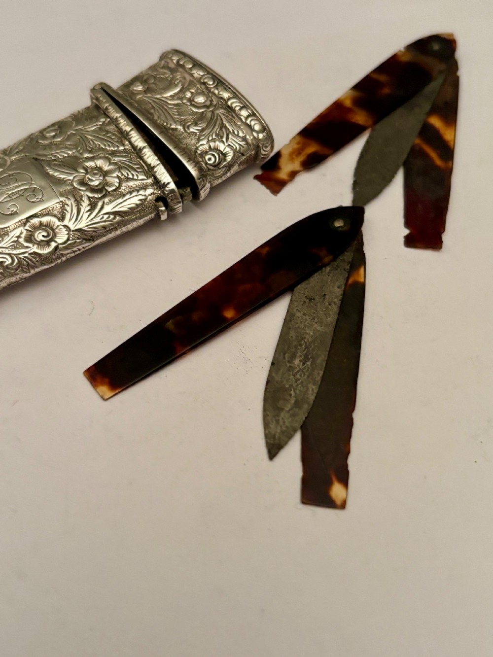 An open William IV sterling silver fleam case with floral chasing, revealing two dark-handled folding blades inside. View VI