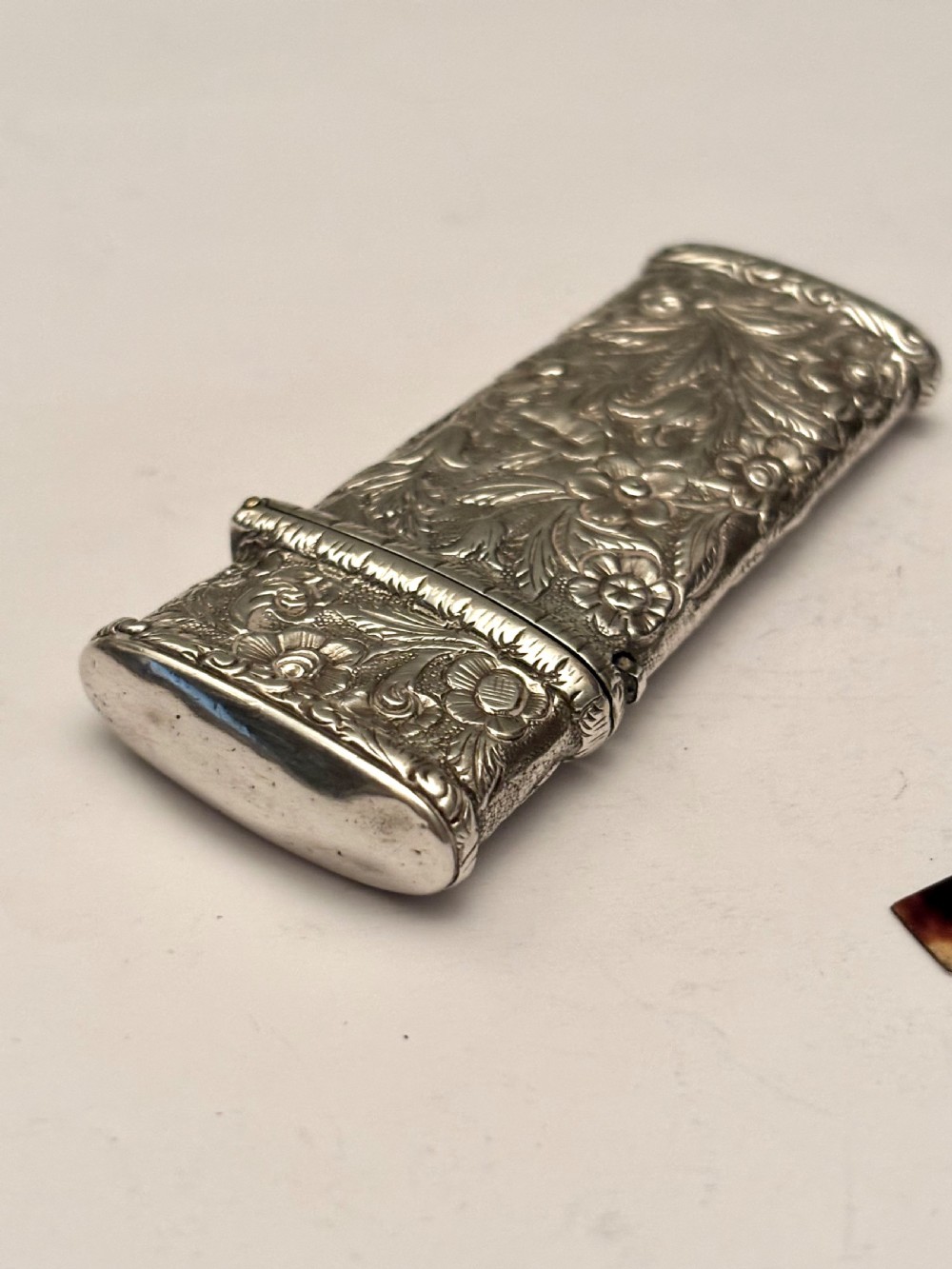An open William IV sterling silver fleam case with floral chasing, revealing two dark-handled folding blades inside. View VII