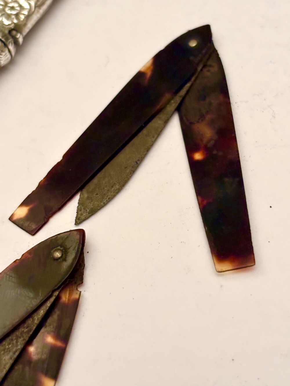 An open William IV sterling silver fleam case with floral chasing, revealing two dark-handled folding blades inside. View IX