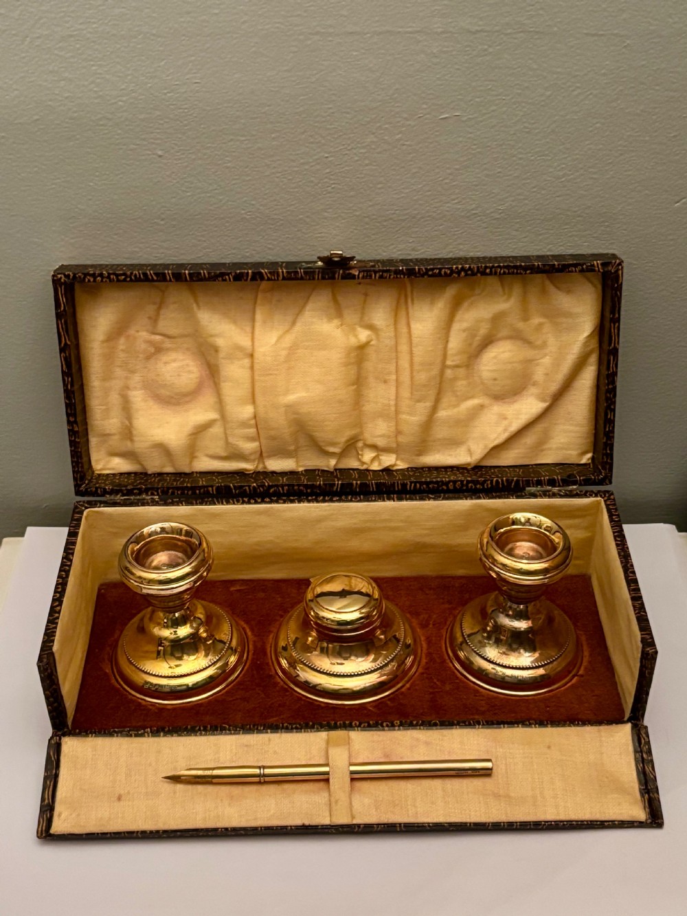 An open fitted presentation box containing two silver gilt candlesticks, a central inkwell, and a dip pen. View IV