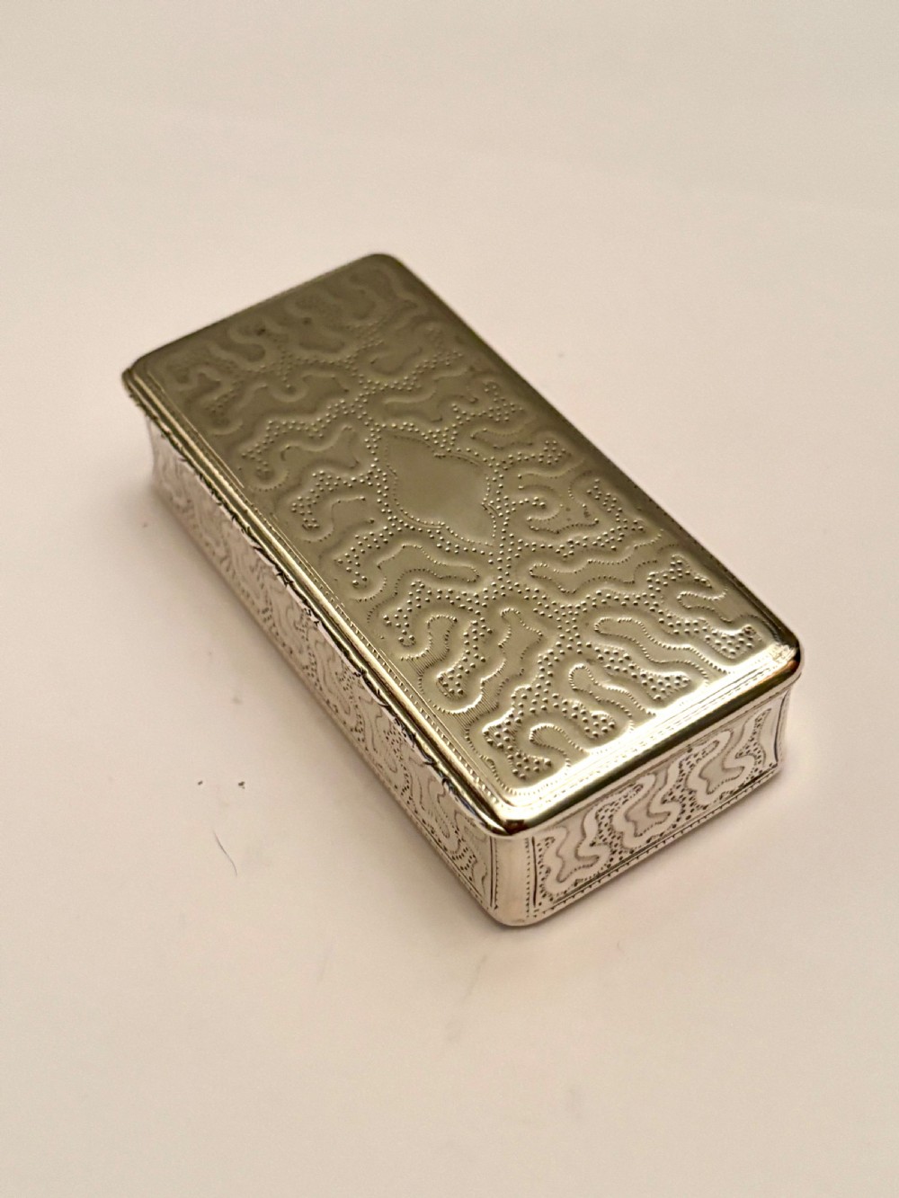 A small rectangular 19th-century French 950 silver gilt snuff box decorated with dense chased scrolling patterns and stippled texture.