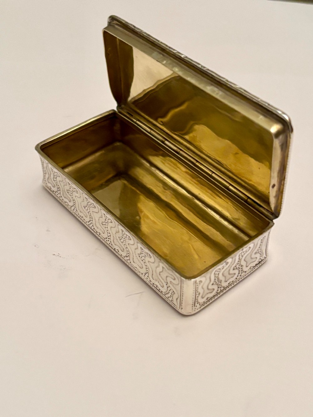 A small rectangular 19th-century French 950 silver gilt snuff box decorated with dense chased scrolling patterns and stippled texture. View II