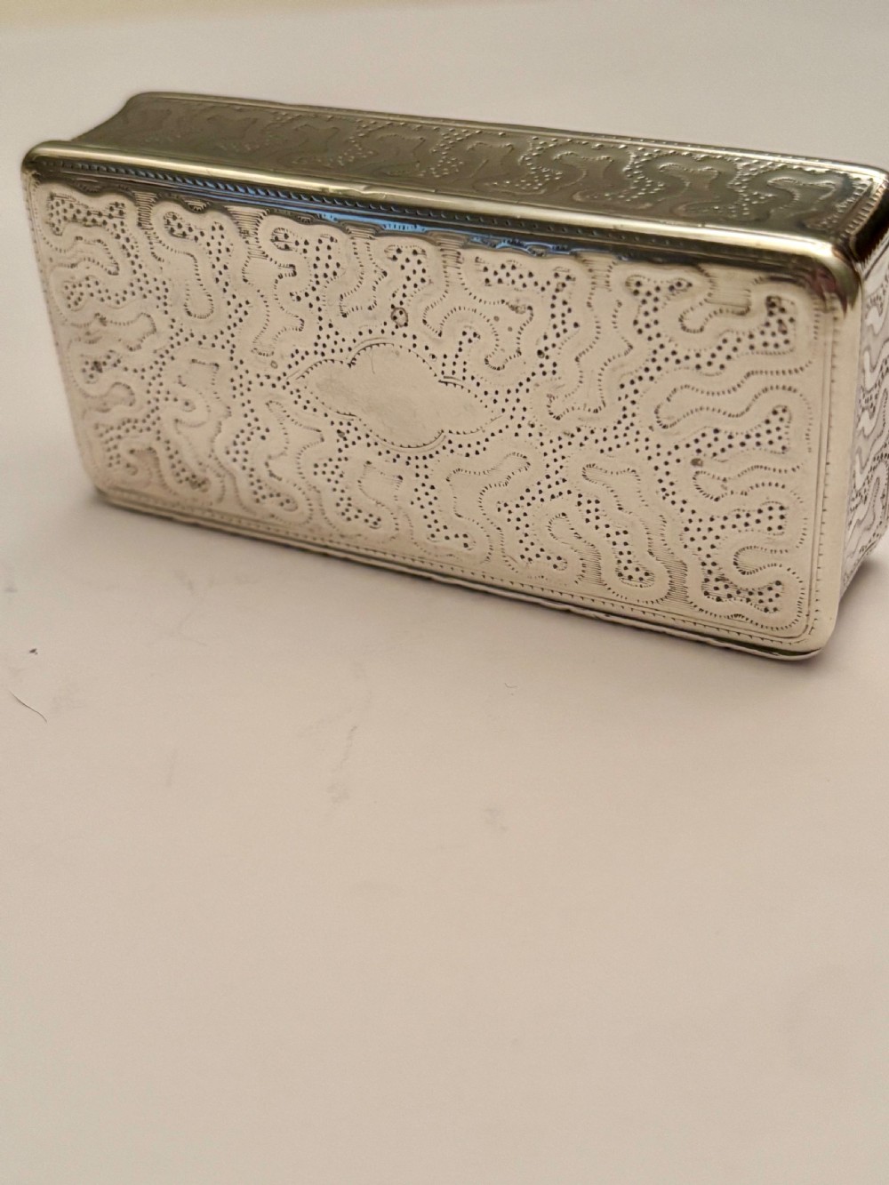 A small rectangular 19th-century French 950 silver gilt snuff box decorated with dense chased scrolling patterns and stippled texture. View V