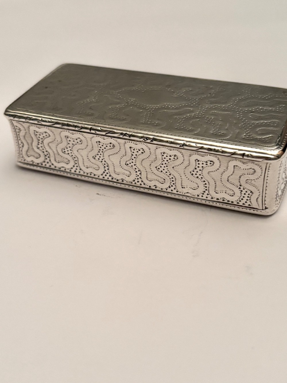 A small rectangular 19th-century French 950 silver gilt snuff box decorated with dense chased scrolling patterns and stippled texture. View VII