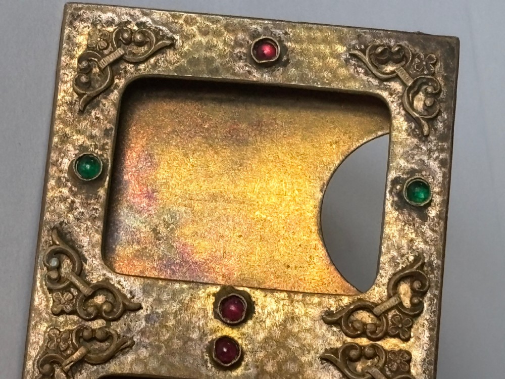 An antique Arts and Crafts double photo frame crafted from hammered gilt brass with applied scroll ornament and colourful cabochon stones containing two black and white portraits. View XI