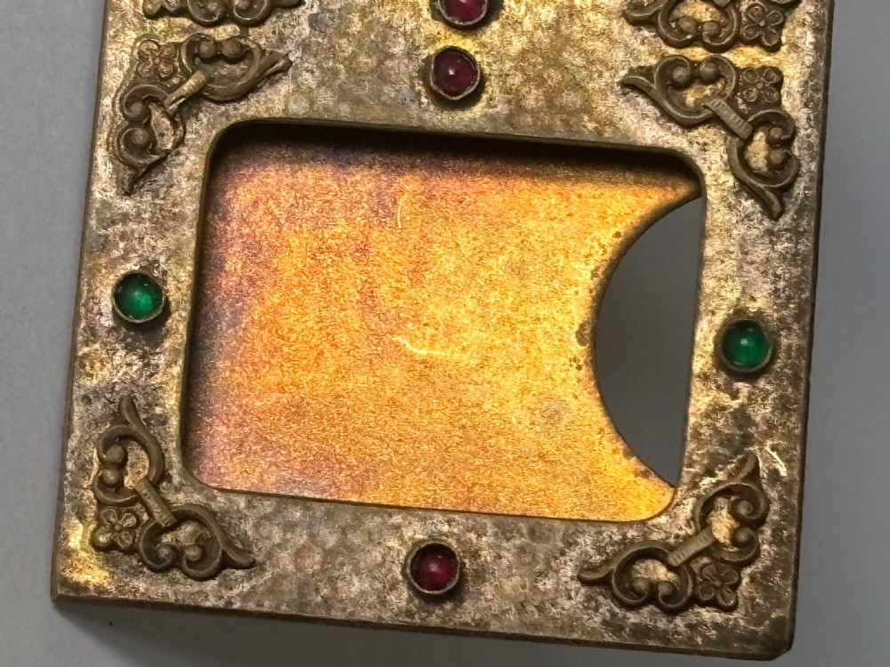 An antique Arts and Crafts double photo frame crafted from hammered gilt brass with applied scroll ornament and colourful cabochon stones containing two black and white portraits. View XII