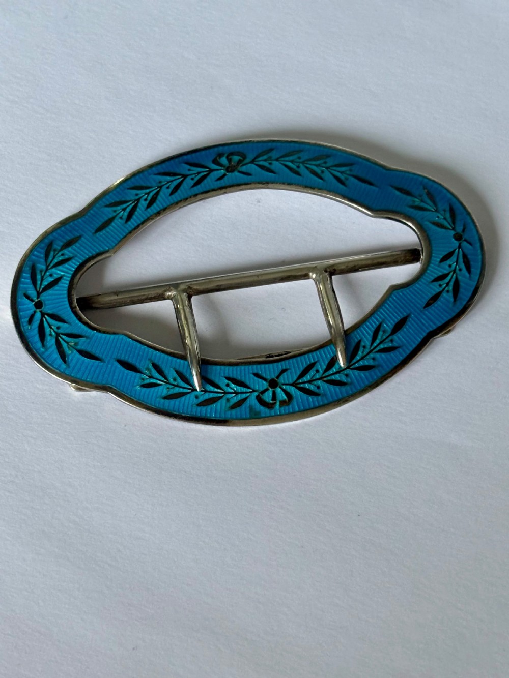An oval Edwardian sterling silver belt buckle decorated with turquoise blue guilloche enamel and black leaf motifs. View II