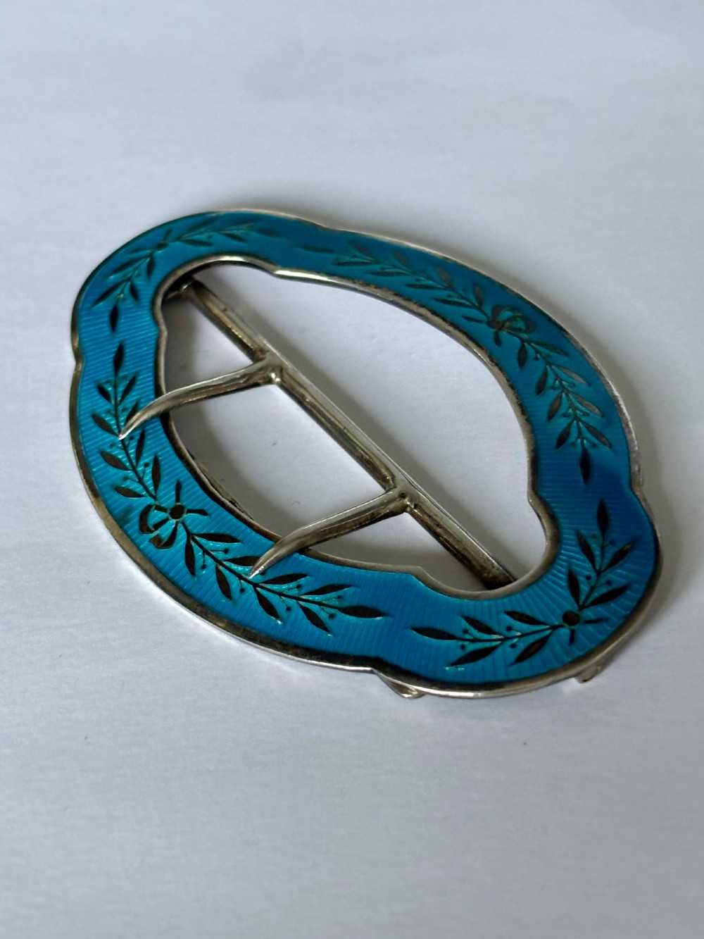An oval Edwardian sterling silver belt buckle decorated with turquoise blue guilloche enamel and black leaf motifs. View IV