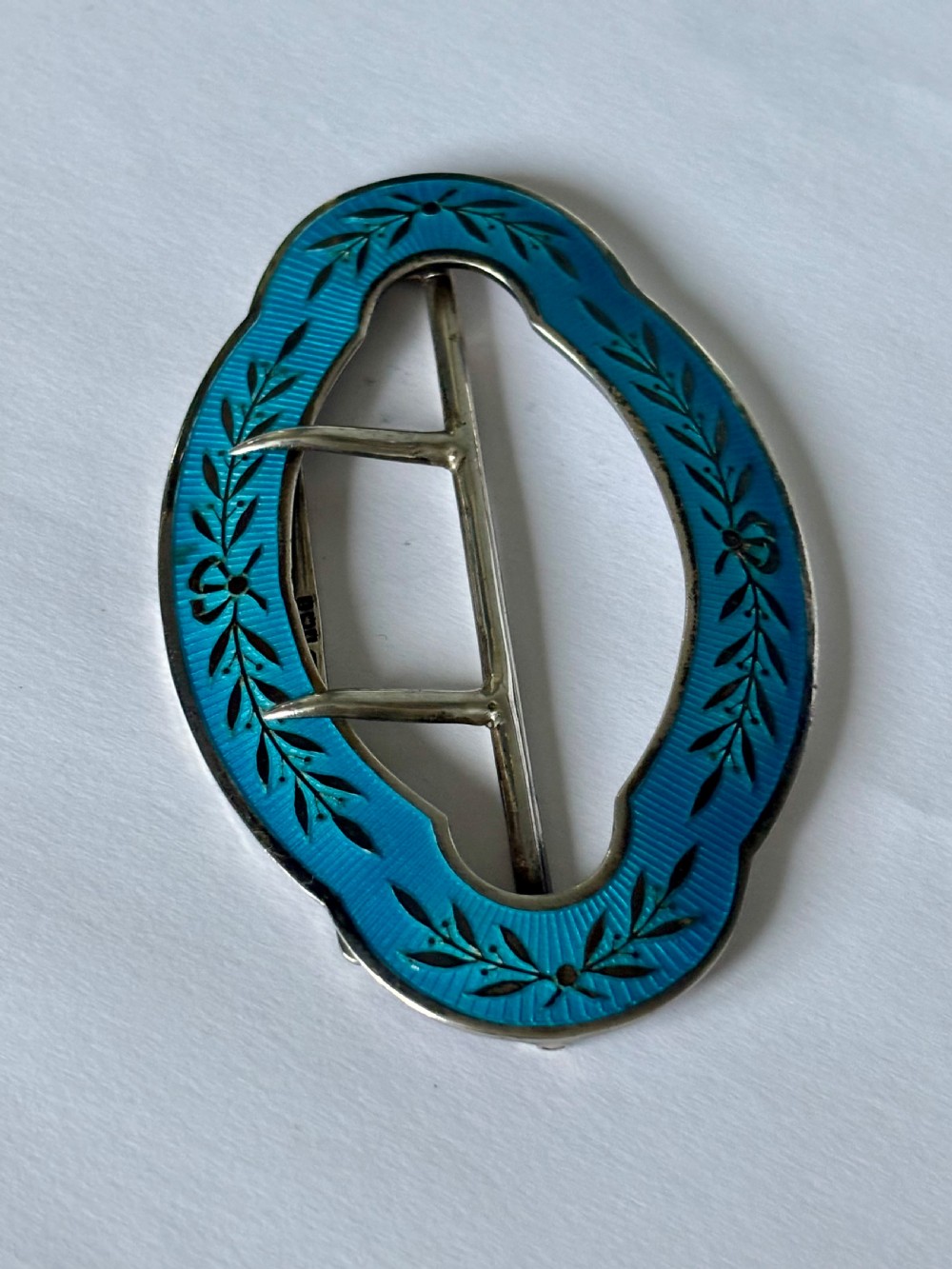 An oval Edwardian sterling silver belt buckle decorated with turquoise blue guilloche enamel and black leaf motifs. View V