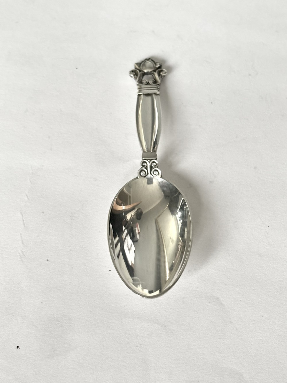 A sterling silver tea caddy spoon featuring a rounded bowl and an acorn motif finial.