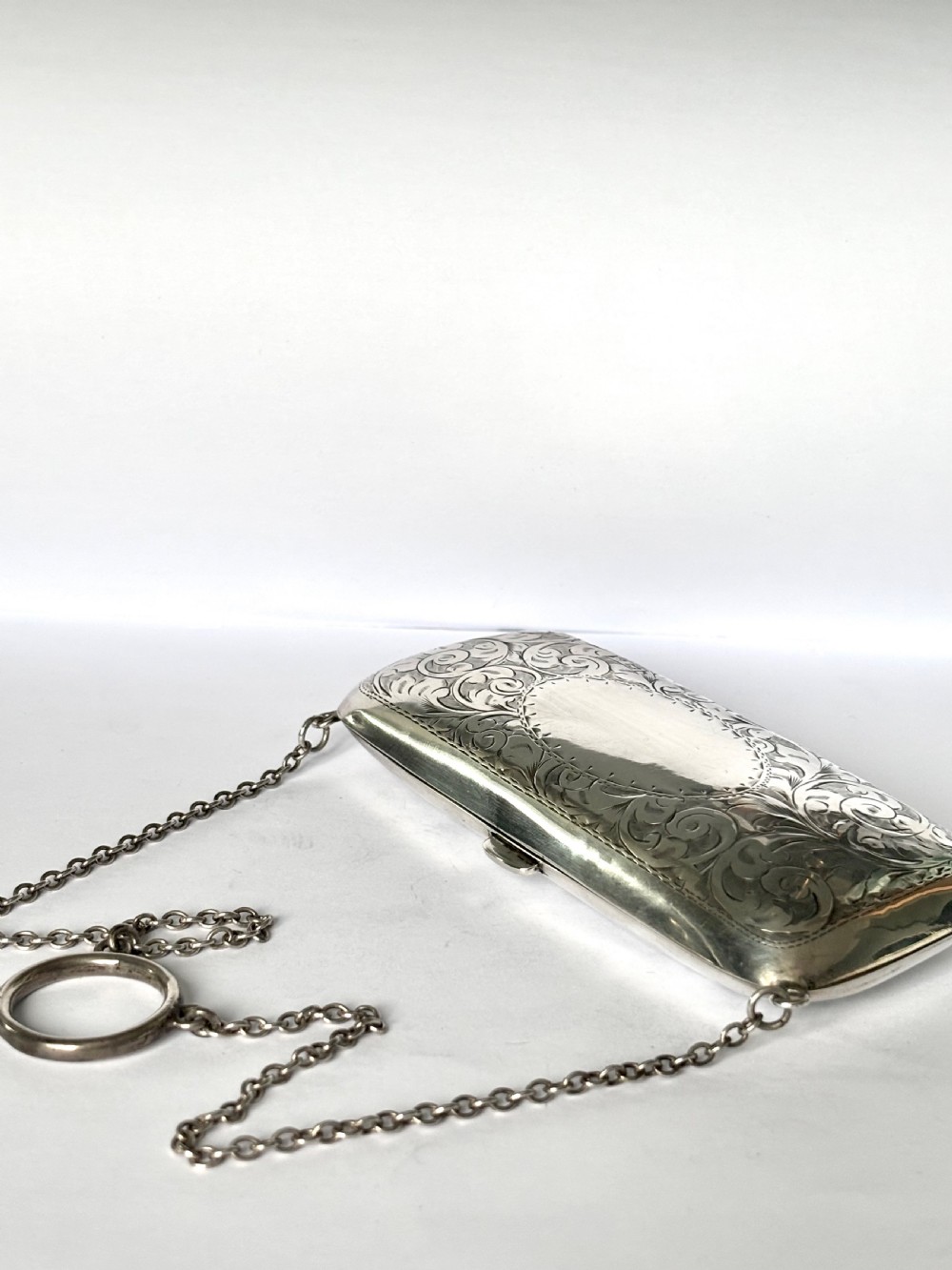 An engraved Art Deco sterling silver purse featuring a fine chain handle, detailed floral scrollwork, and a central polished oval cartouche. View VII