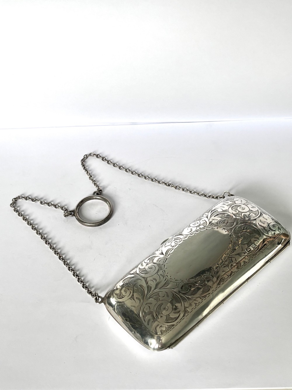 An engraved Art Deco sterling silver purse featuring a fine chain handle, detailed floral scrollwork, and a central polished oval cartouche. View X
