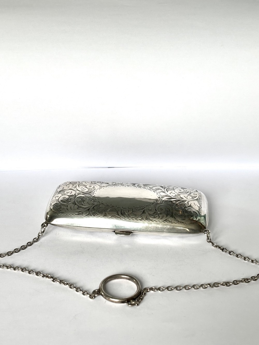 An engraved Art Deco sterling silver purse featuring a fine chain handle, detailed floral scrollwork, and a central polished oval cartouche. View XIII