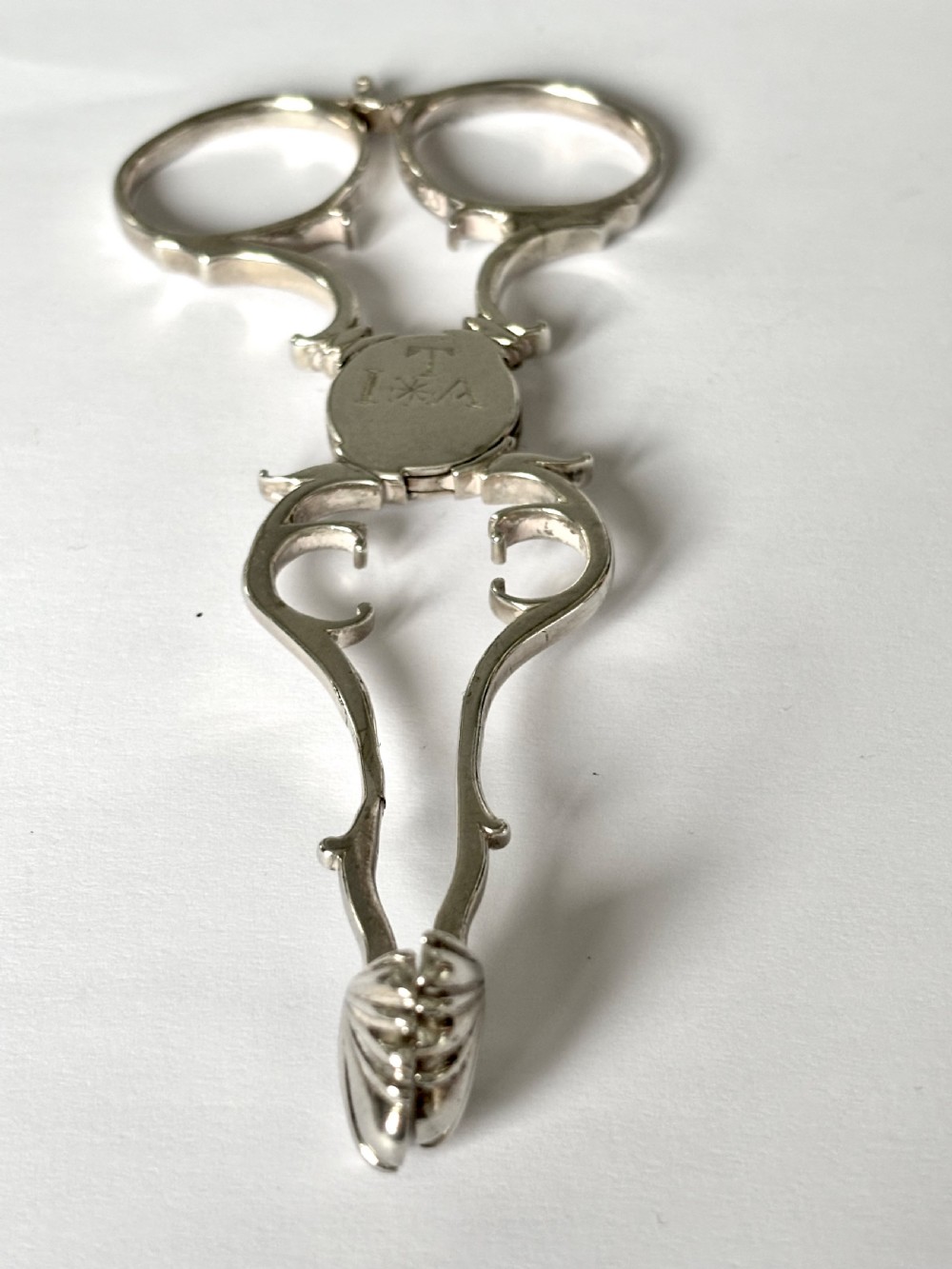 A pair of Georgian sterling silver sugar nips featuring scissor-action finger loops, scroll arms, and shell-shaped grips. View VI