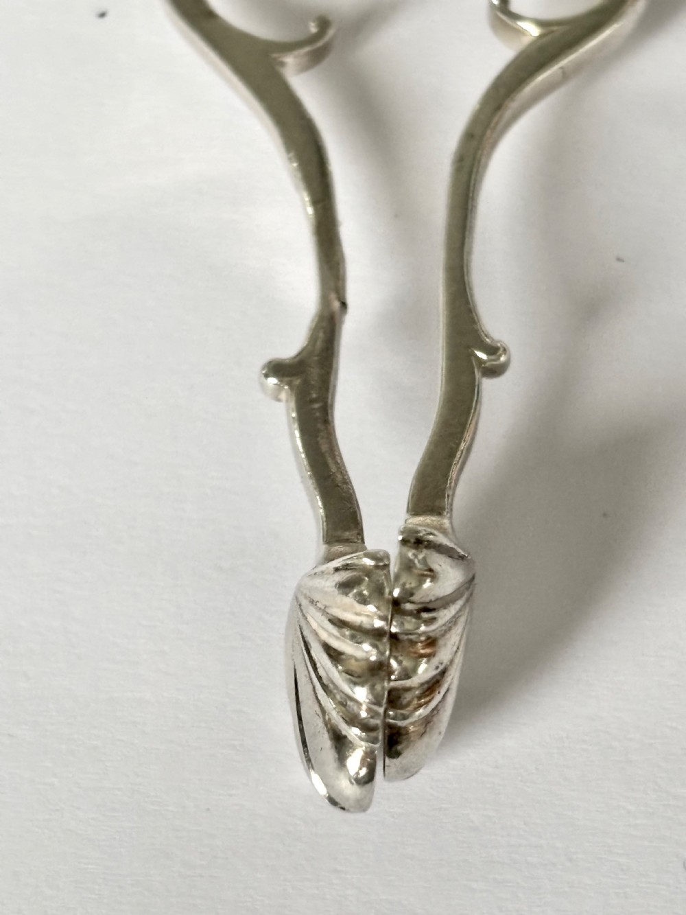 A pair of Georgian sterling silver sugar nips featuring scissor-action finger loops, scroll arms, and shell-shaped grips. View IX