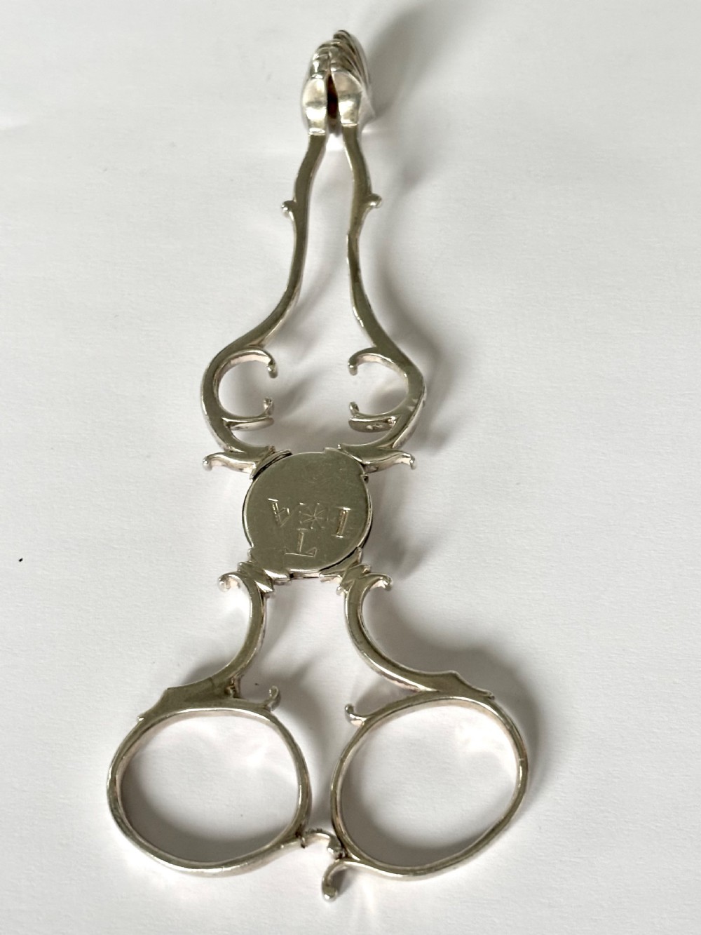 A pair of Georgian sterling silver sugar nips featuring scissor-action finger loops, scroll arms, and shell-shaped grips. View XI