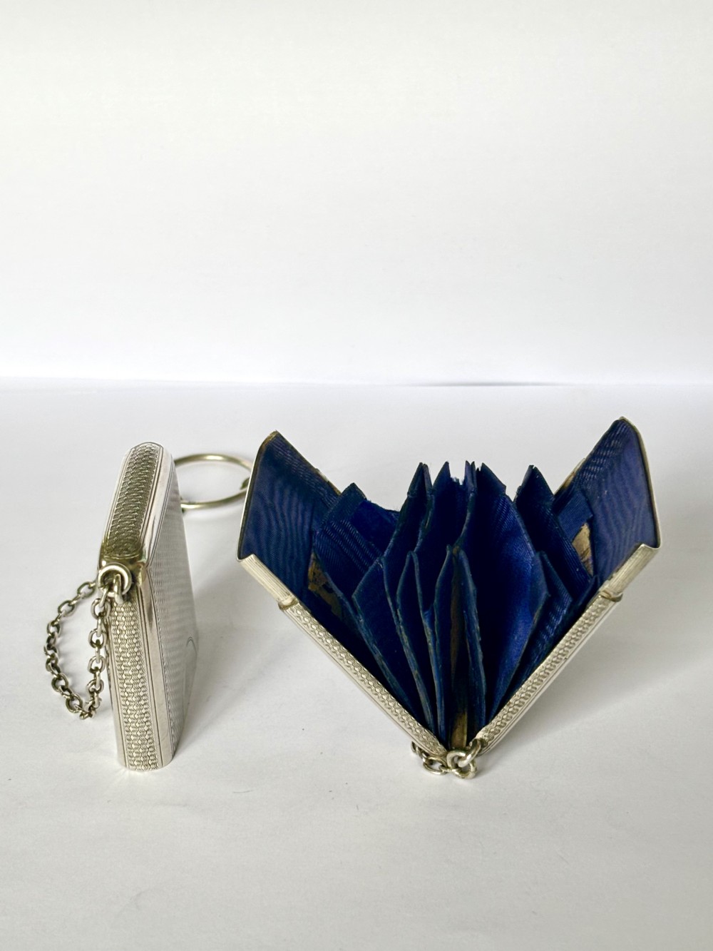 A Victorian sterling silver purse with engine-turned geometric engraving, shown open with a blue silk concertina lining beside a detachable silver case.