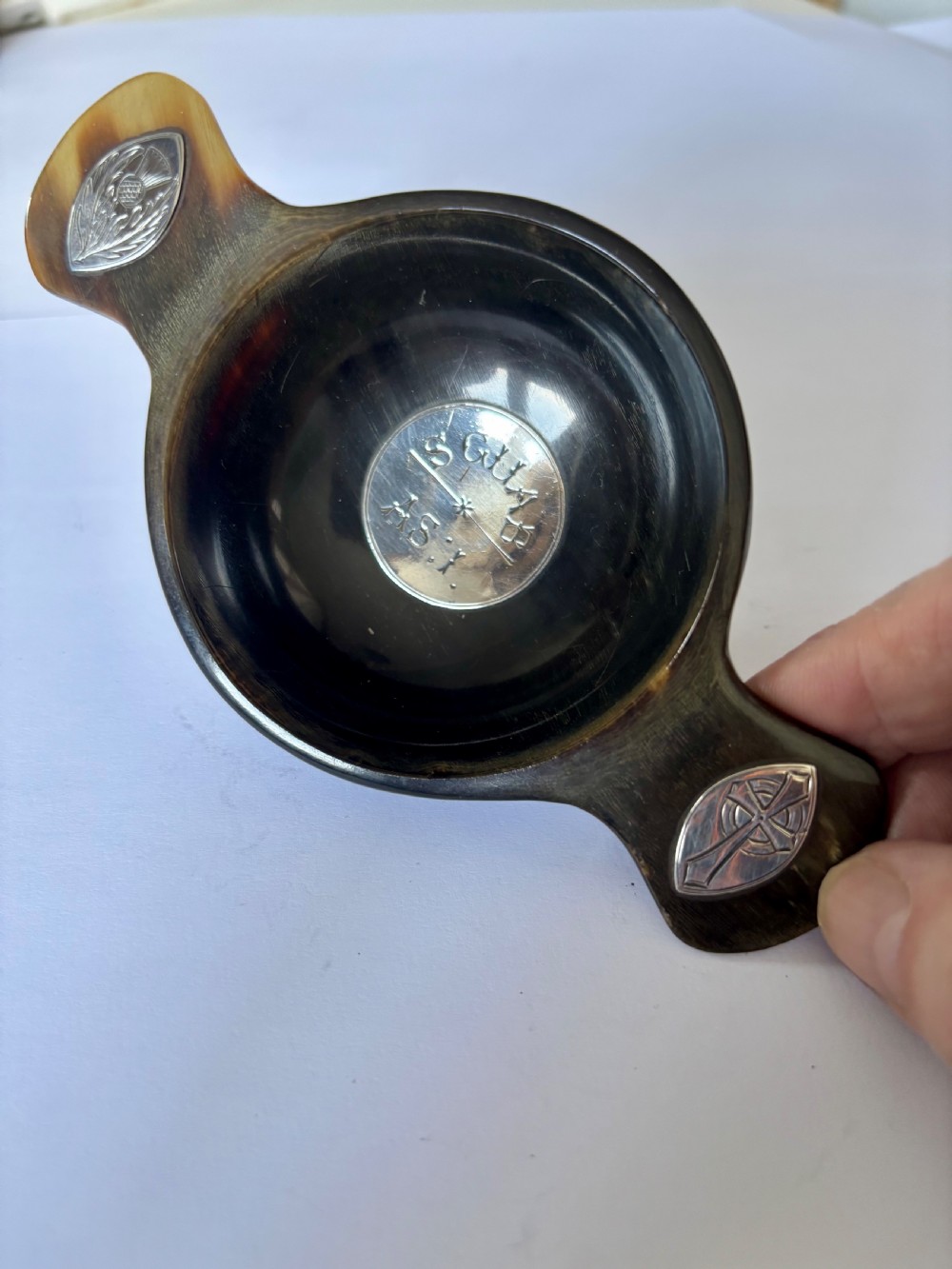 An antique Scottish horn quaich featuring carved lug handles with hallmarked silver thistle and Celtic cross mounts, and an inscribed silver central boss inside the bowl.