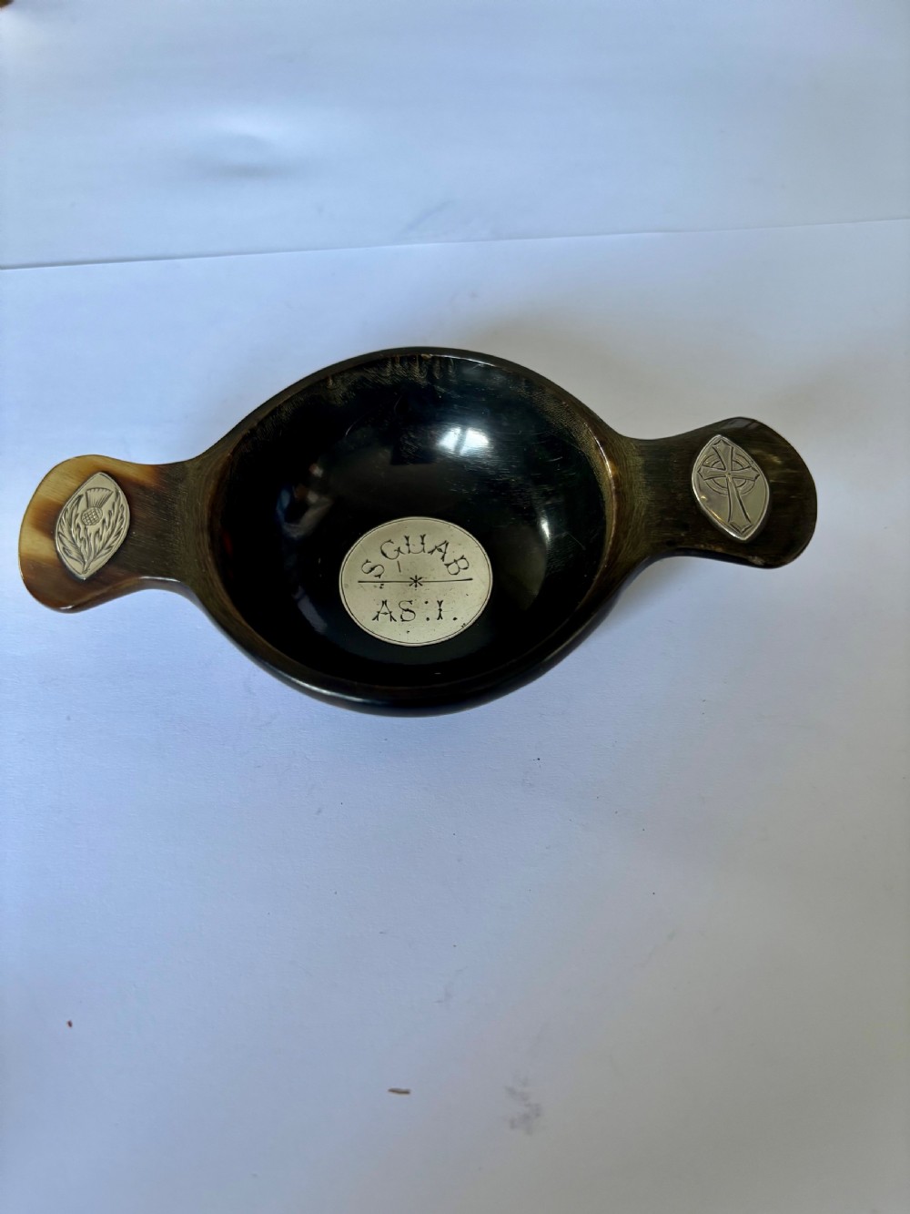 An antique Scottish horn quaich featuring carved lug handles with hallmarked silver thistle and Celtic cross mounts, and an inscribed silver central boss inside the bowl. View II
