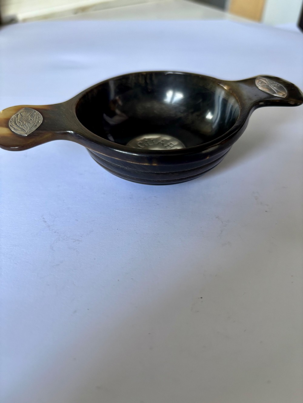 An antique Scottish horn quaich featuring carved lug handles with hallmarked silver thistle and Celtic cross mounts, and an inscribed silver central boss inside the bowl. View III