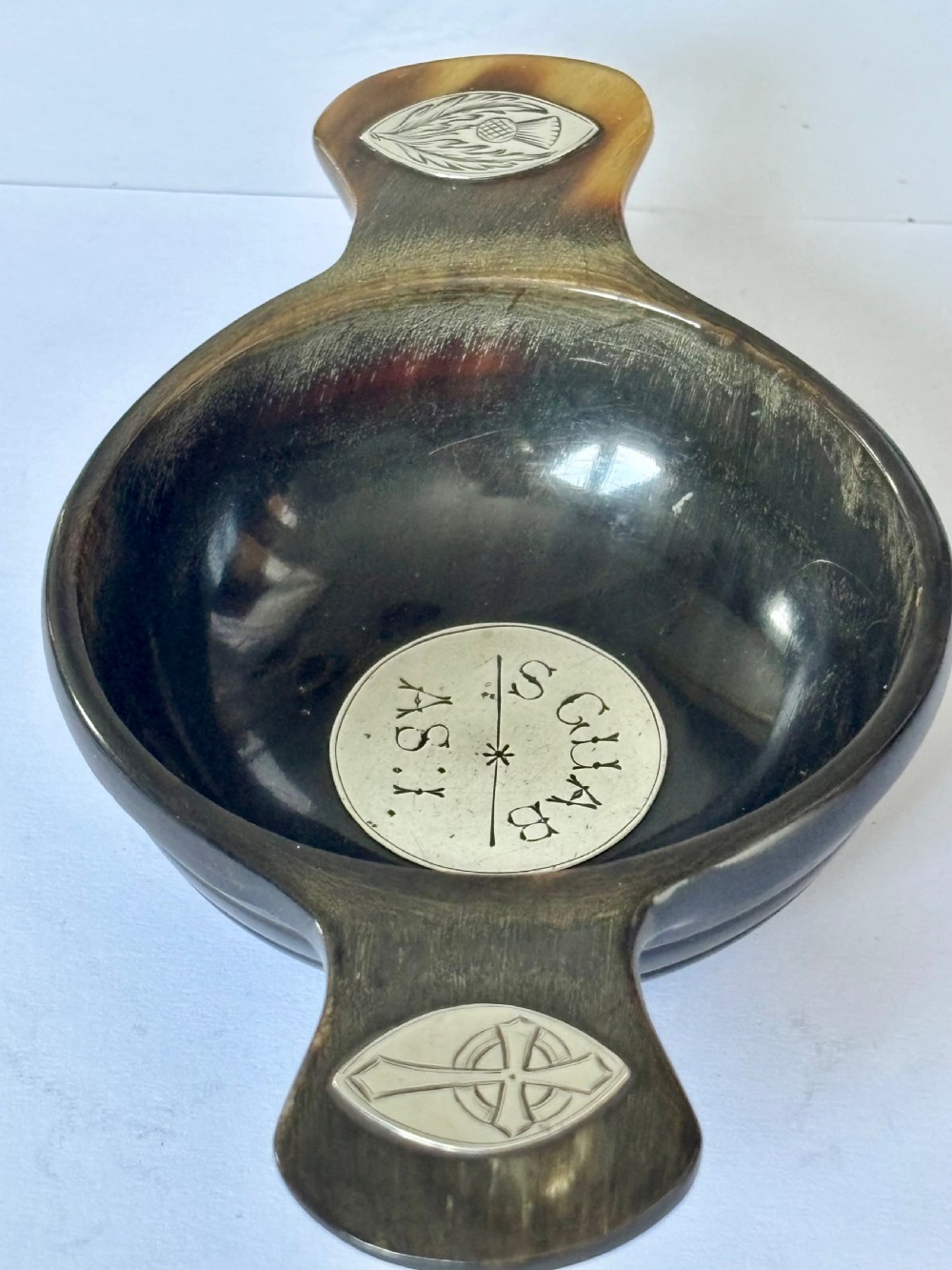 An antique Scottish horn quaich featuring carved lug handles with hallmarked silver thistle and Celtic cross mounts, and an inscribed silver central boss inside the bowl. View IV