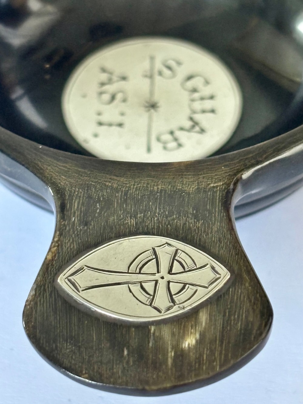 An antique Scottish horn quaich featuring carved lug handles with hallmarked silver thistle and Celtic cross mounts, and an inscribed silver central boss inside the bowl. View VI