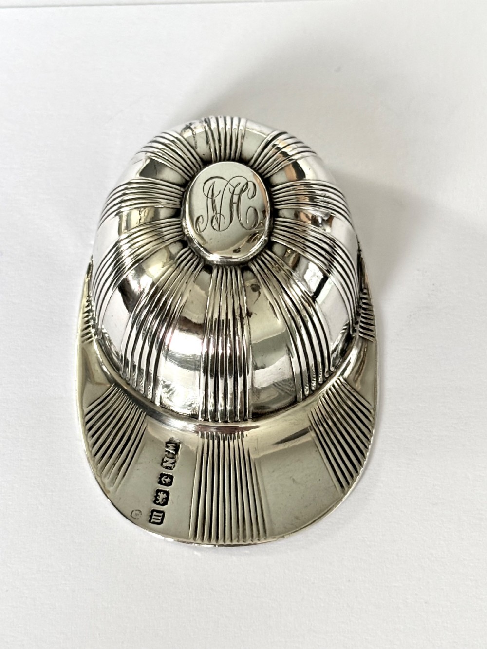 A solid sterling silver caddy spoon shaped like a peaked jockey cap with fluted panel detailing and British hallmarks along the brim. View IV