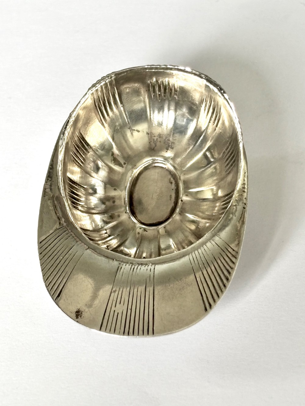 A solid sterling silver caddy spoon shaped like a peaked jockey cap with fluted panel detailing and British hallmarks along the brim. View V