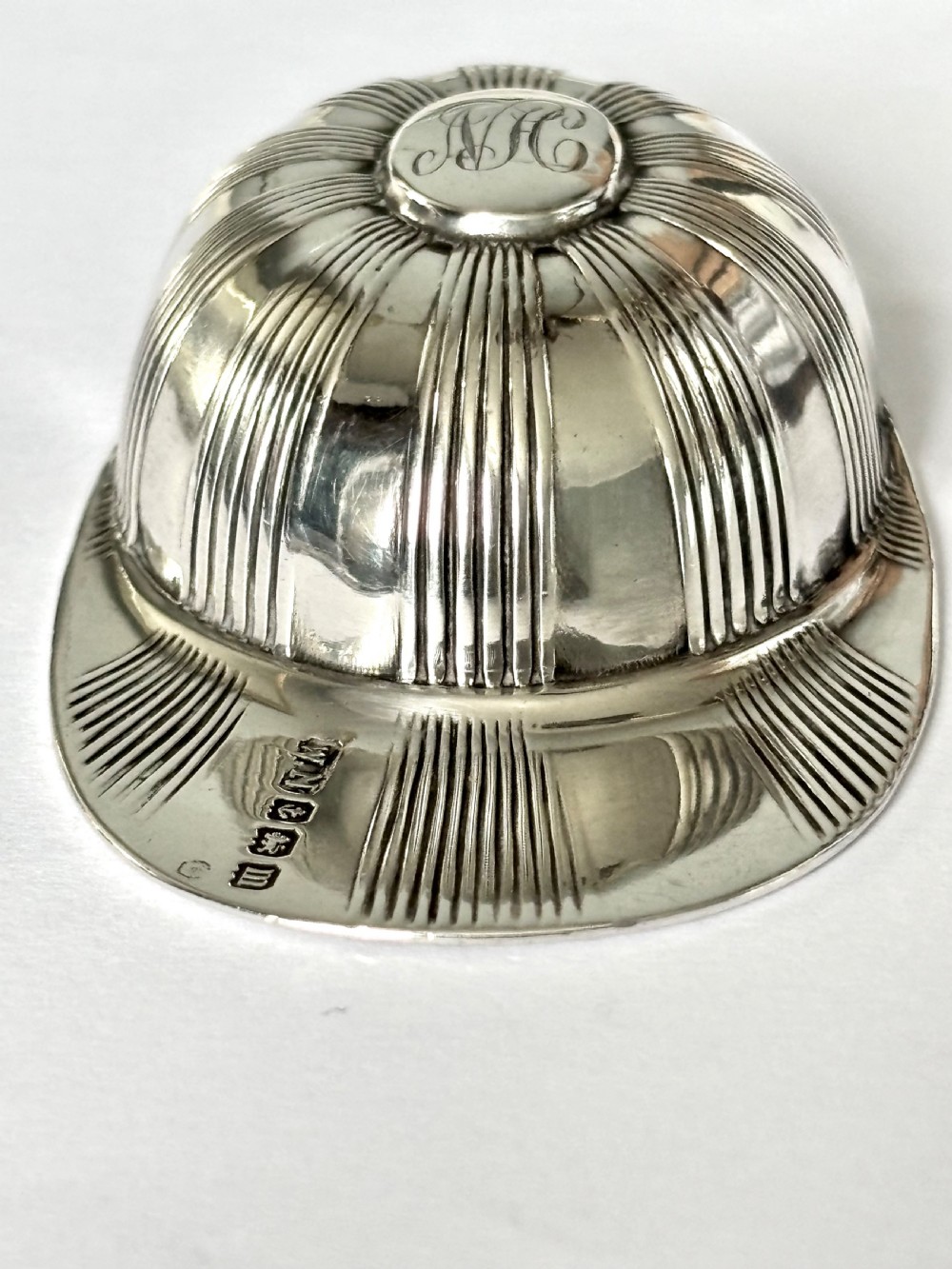 A solid sterling silver caddy spoon shaped like a peaked jockey cap with fluted panel detailing and British hallmarks along the brim. View VI