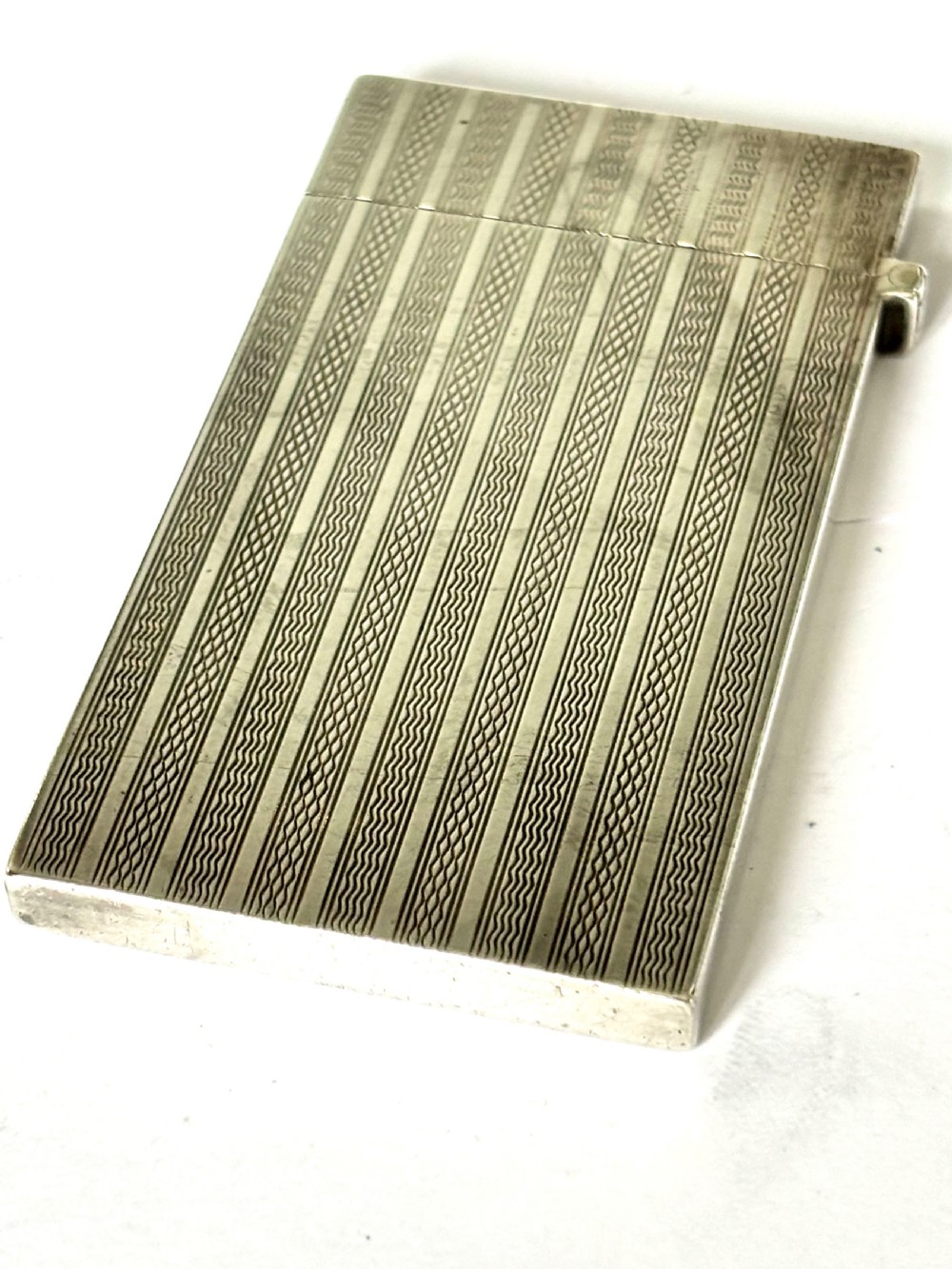 An Edwardian sterling silver slimline calling card case featuring vertical engine-turned stripes and a central oval monogram cartouche. View V